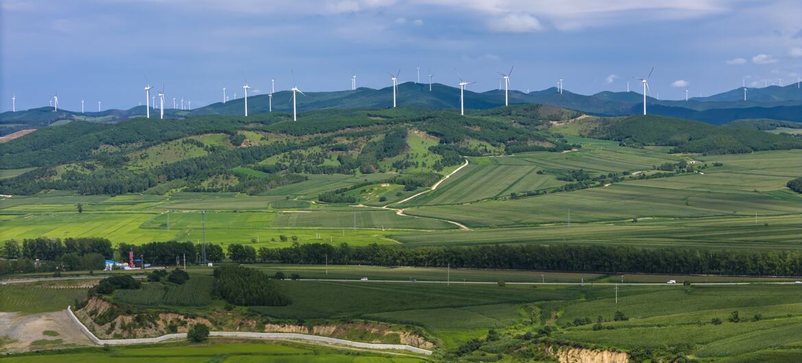 风力发电机在部分云层天空下划分绿色的山丘和滚动的农田,